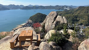 Una mesa de picnic de madera sobre una ladera rocosa con vistas a una zona costera, montañas y un puente a lo lejos.