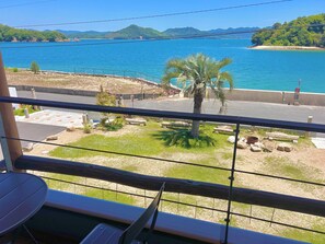 A balcony with a view of a body of water, a palm tree, and a rocky area with a bench. - East Villa Shimanami right in front of the sea（petOK,BBQ,Max7,bike,SUP,kayak) (Onomichi)