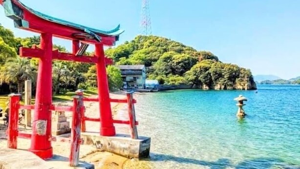 Un torii rojo en una ubicación costera, con aguas cristalinas y una isla rocosa al fondo.
