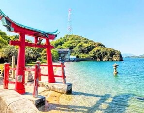 A red torii gate at a coastal location with clear water and a rocky island in the background. - East Villa Shimanami right in front of the sea（petOK,BBQ,Max7,bike,SUP,kayak) (Onomichi)