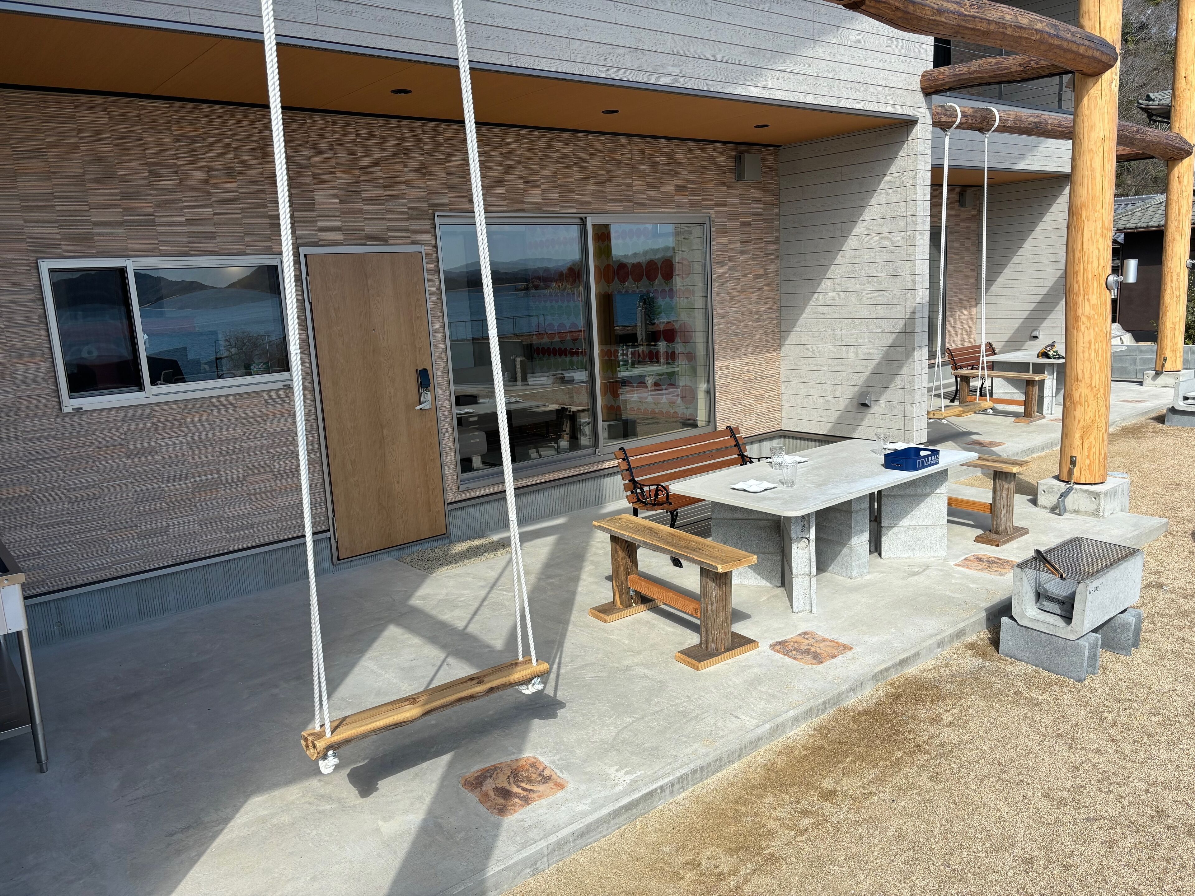 An outdoor patio with a swing set, a table with chairs, and a wooden bench.