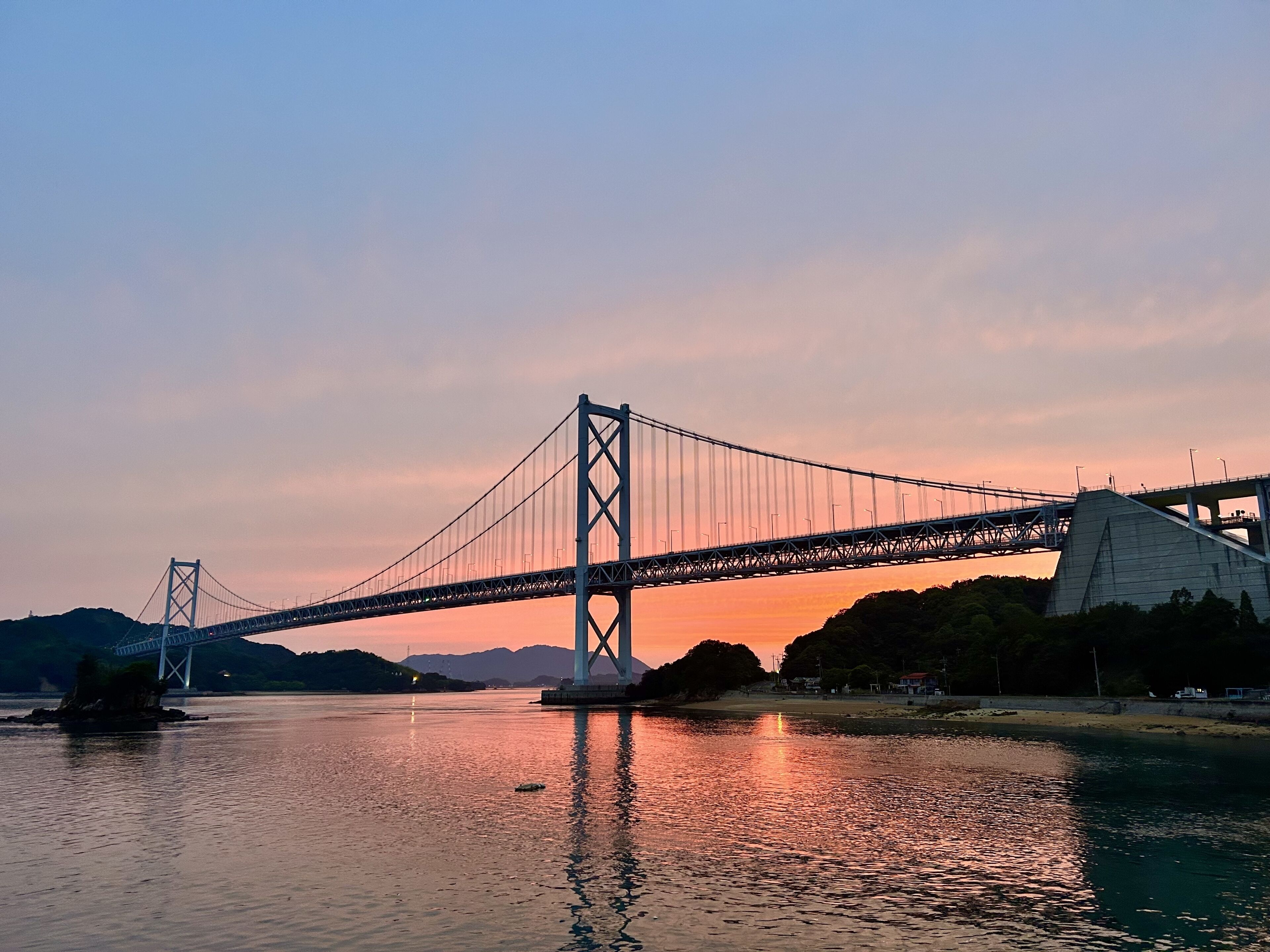 Un pont suspendu enjambant une étendue d’eau, avec un coucher de soleil en arrière-plan.