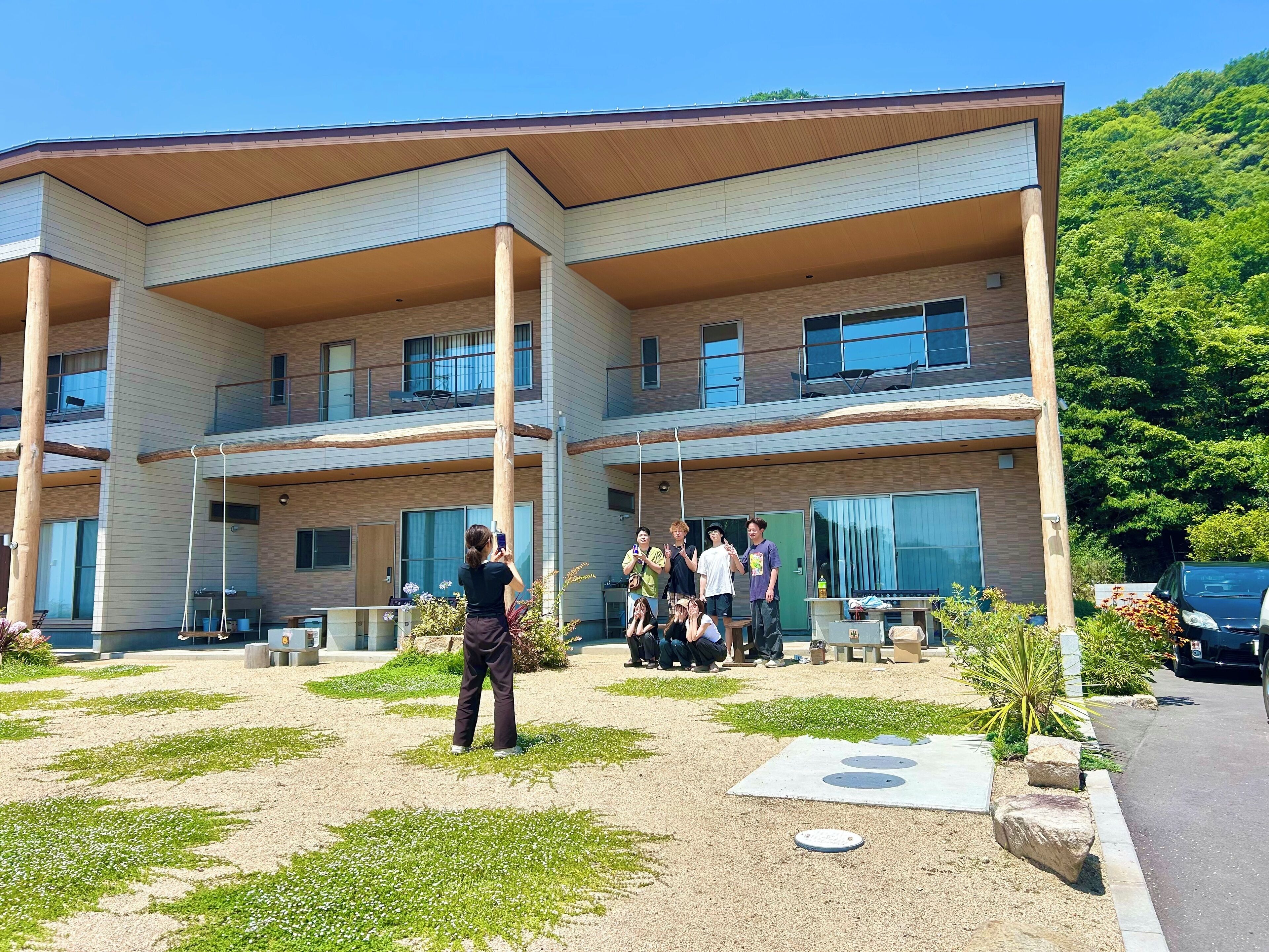 Ein mehrgeschossiges Gebäude mit moderner Architektur, das einen überdachten Außenbereich mit Sitzgelegenheiten und einen kleinen Garten umfasst.
