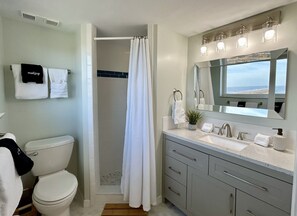 A bathroom with a toilet, a shower with a curtain, a sink with a mirror, and towels on the wall. - Oceanfront Penthouse Suite, 2 King Beds, Exquisite Beach Views, Newly Renovated (Fernandina Beach)