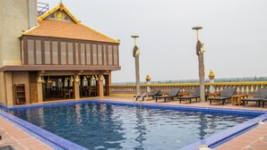 A swimming pool with a tiled border, a building with a tiled roof, and a railing with chairs. - Puok hotel & Resort (Puok)