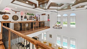 A spacious interior with a wooden ceiling, a balcony with a railing, and a pool visible through the windows. - Mini Golf, Splash Pad, Indoor Playground, Movie Theatre & Summer Kitchen (Kissimmee)