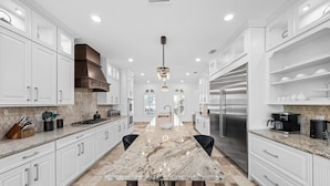A modern kitchen with white cabinetry, a marble island, stainless steel appliances, and a pendant light. - Mini Golf, Splash Pad, Indoor Playground, Movie Theatre & Summer Kitchen (Kissimmee)