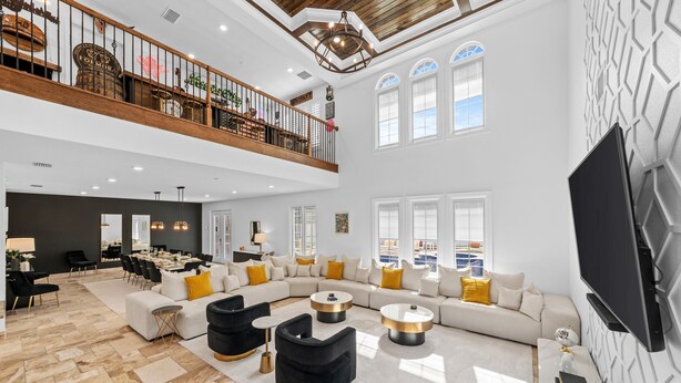 A spacious living area with a high ceiling, a balcony with wooden railings, and a large flat-screen TV mounted on the wall. - Mini Golf, Splash Pad, Indoor Playground, Movie Theatre & Summer Kitchen (Kissimmee)