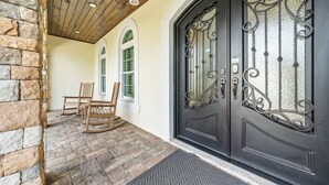 A stone exterior wall, a wooden ceiling, a black door with decorative metalwork, and a rocking chair outside. - Mini Golf, Splash Pad, Indoor Playground, Movie Theatre & Summer Kitchen (Kissimmee)