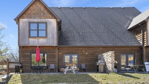 Una cabaña de troncos con una amplia terraza, mobiliario exterior y una chimenea de piedra.