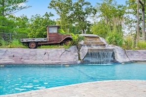 Una piscina con una cascada y un camión antiguo estacionado cerca.