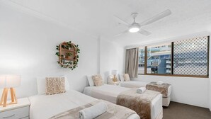 A hotel room with two beds, a ceiling fan, a window with a view, and a small plant on the wall.