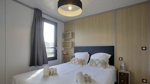 Un lit bien fait, avec des serviettes, une table de chevet avec une lampe et une fenêtre avec des rideaux.