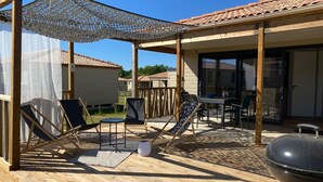 Une terrasse en bois avec des chaises longues, un barbecue et un patio couvert comprenant une table et des chaises.