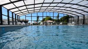 Une piscine intérieure dotée d’un toit en verre, de chaises longues et offrant une vue sur les environs.
