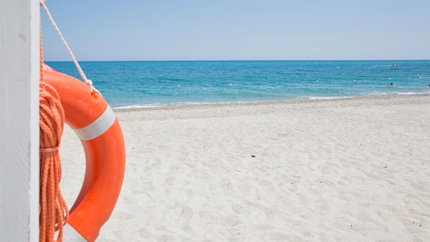 Ein Strand mit einem Rettungsbojen an einem Seil, klarem, blauem Wasser und einem sandigen Ufer.