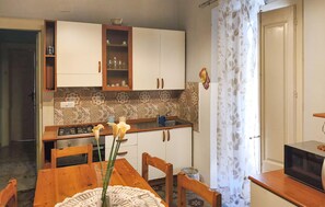 A compact kitchen with a gas stove, wooden cabinets, a patterned backsplash, and a dining area with a table and chairs.