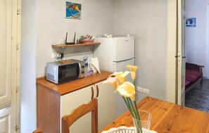 A compact kitchen with a microwave, refrigerator, and a wooden dining table with chairs.