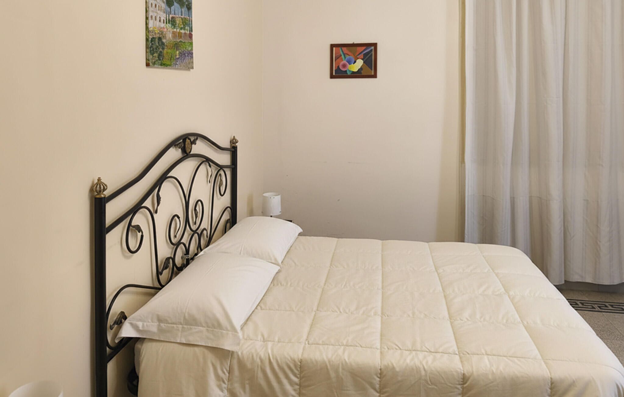 A single bed with a headboard, a bedside table with a lamp, and two framed artworks on the wall.