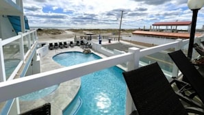 A rooftop pool with lounge chairs, a view of the beach, and a building with a red roof. - Retro Ocean Front, Private Deck, Pool, Elevator, Linens  (Wildwood Crest)