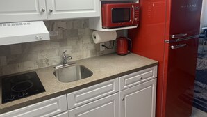 A kitchen with white cabinets, a red Galanz refrigerator, a red microwave, a stainless steel sink, and a black induction cooktop. - Retro Ocean Front, Private Deck, Pool, Elevator, Linens  (Wildwood Crest)