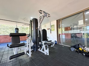 Un gimnasio con equipo de levantamiento de pesas, un saco de boxeo y una puerta de vidrio que da al exterior.