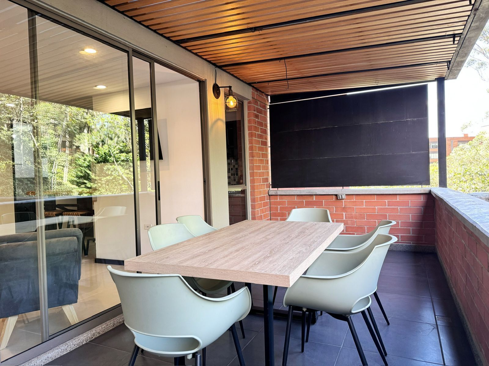 A modern outdoor dining area with a wooden table and white chairs, a brick wall, and a glass partition.