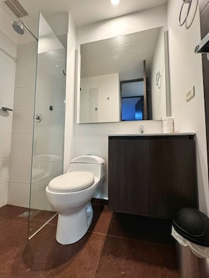 Un baño moderno con cabina de ducha de vidrio, inodoro blanco y tocador de madera oscura.