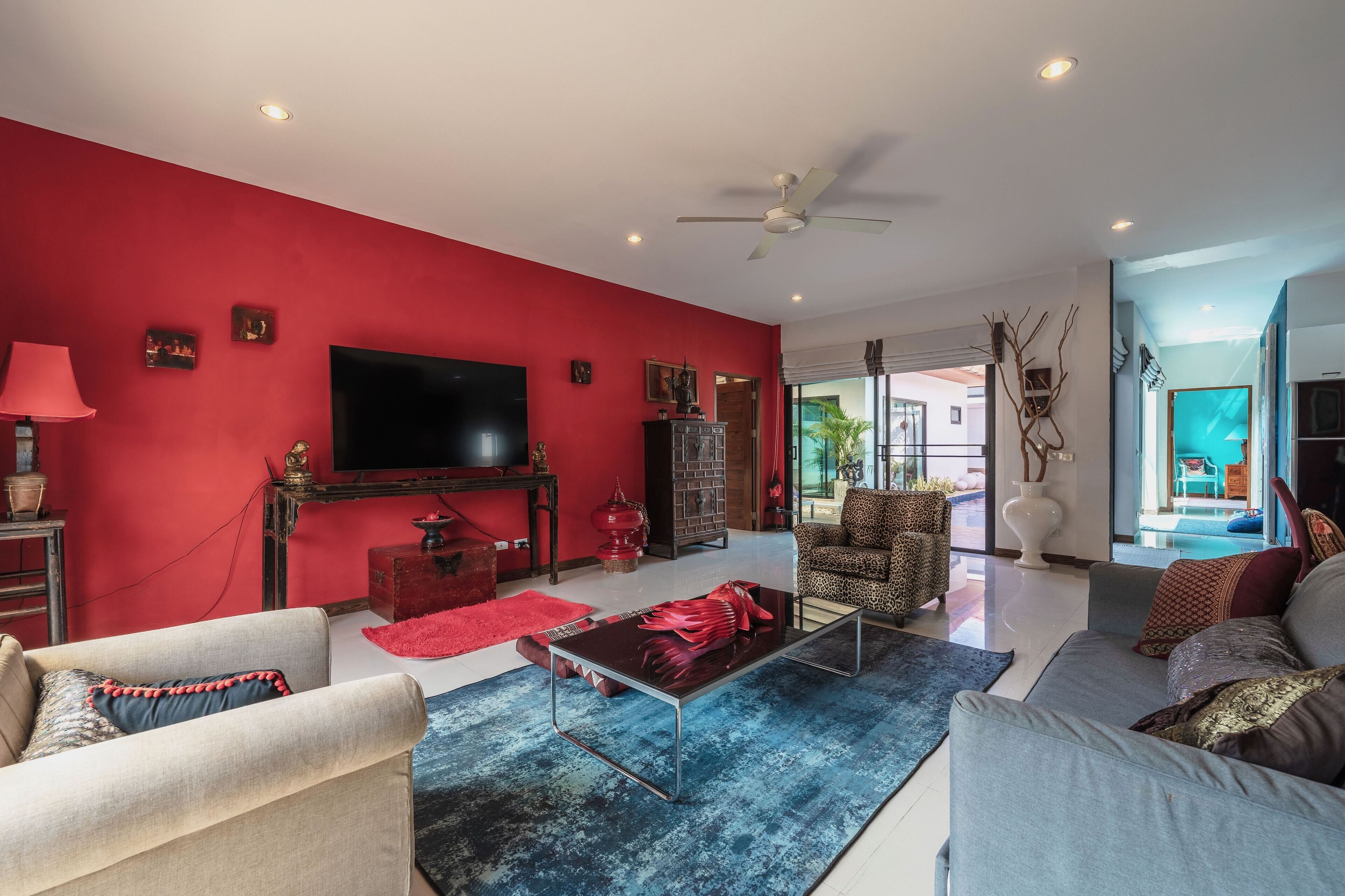 Un salon avec un mur rouge, un téléviseur à écran plat, un ventilateur de plafond et une grande fenêtre.