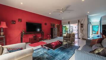 Un salon avec un mur rouge, un téléviseur à écran plat, un ventilateur de plafond et une grande fenêtre.