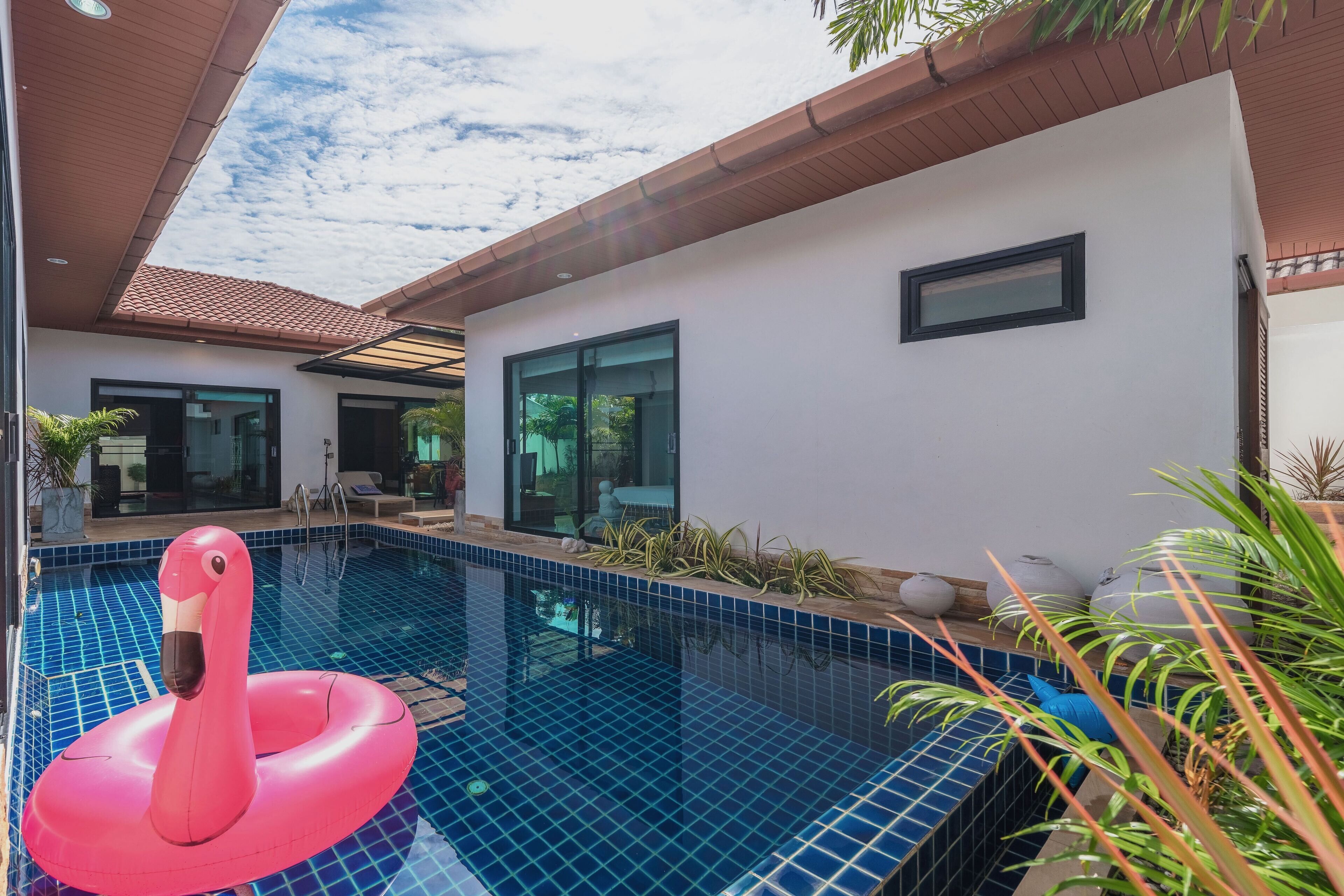 A modern house with a swimming pool, a pink flamingo float, and a patio area with plants.