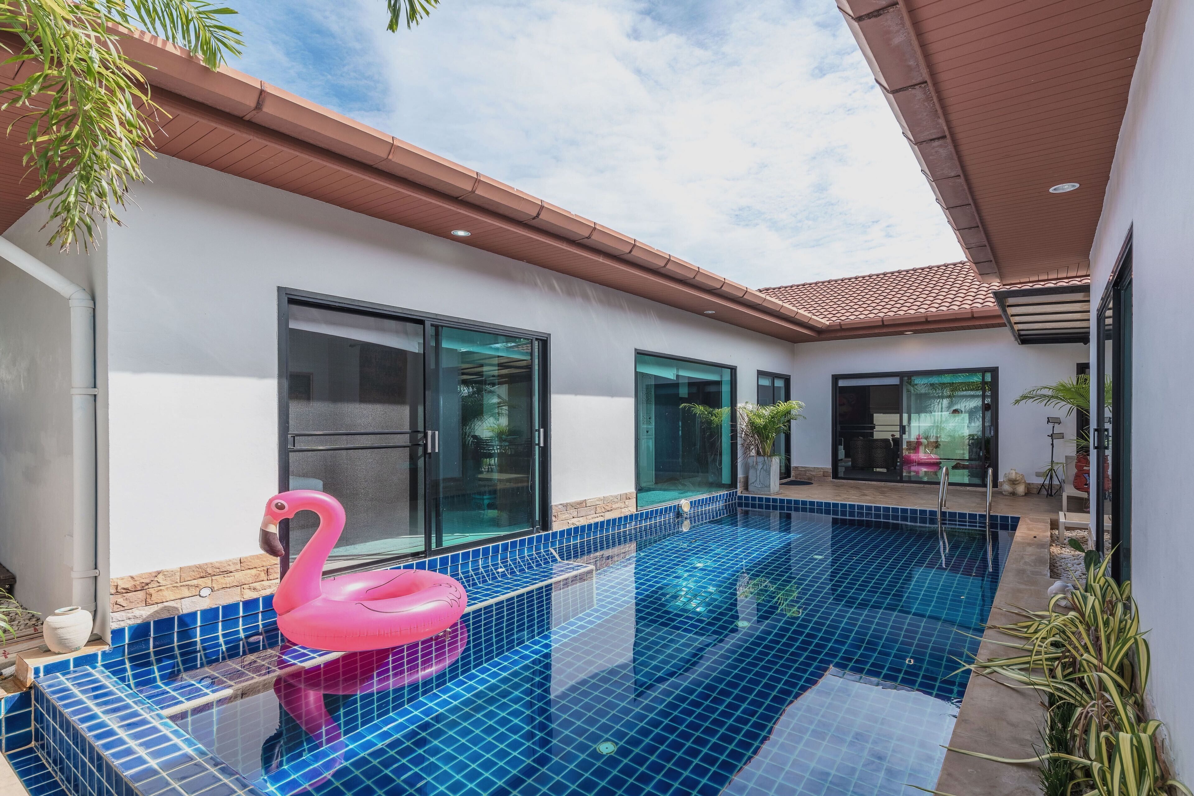 A modern outdoor pool with blue tiles, a pink flamingo float, and a potted plant.