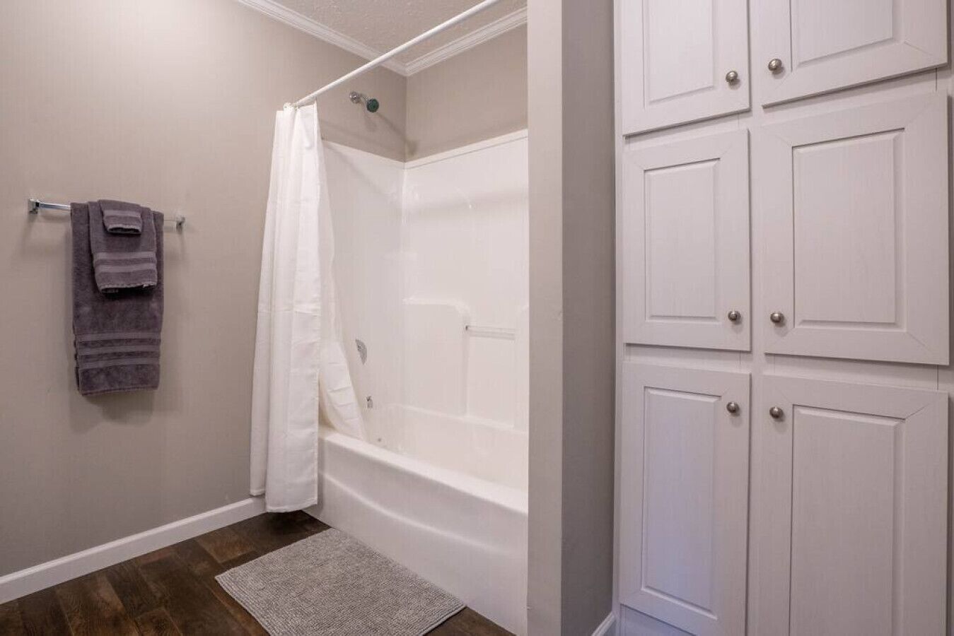 A bathroom with a bathtub, a shower curtain, a towel rack with towels, and a set of white cabinets.