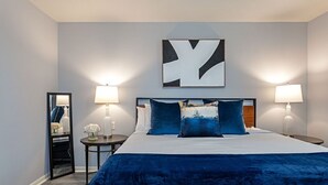 Een hotelkamer met een groot bed, twee bedlampen, een spiegel en een abstract kunstwerk aan de muur.