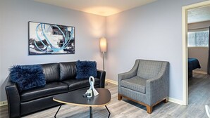 Een moderne woonkamer met een zwarte leren bank, een grijze fauteuil, een bijzettafeltje en een vloerlamp.