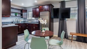 Een moderne keuken met donkerhouten kastjes, een roestvrijstalen koelkast, een flatscreen televisie en een eethoek met een ronde tafel en vier stoelen.
