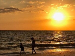 Atardecer sobre el océano con dos personas caminando por la playa.