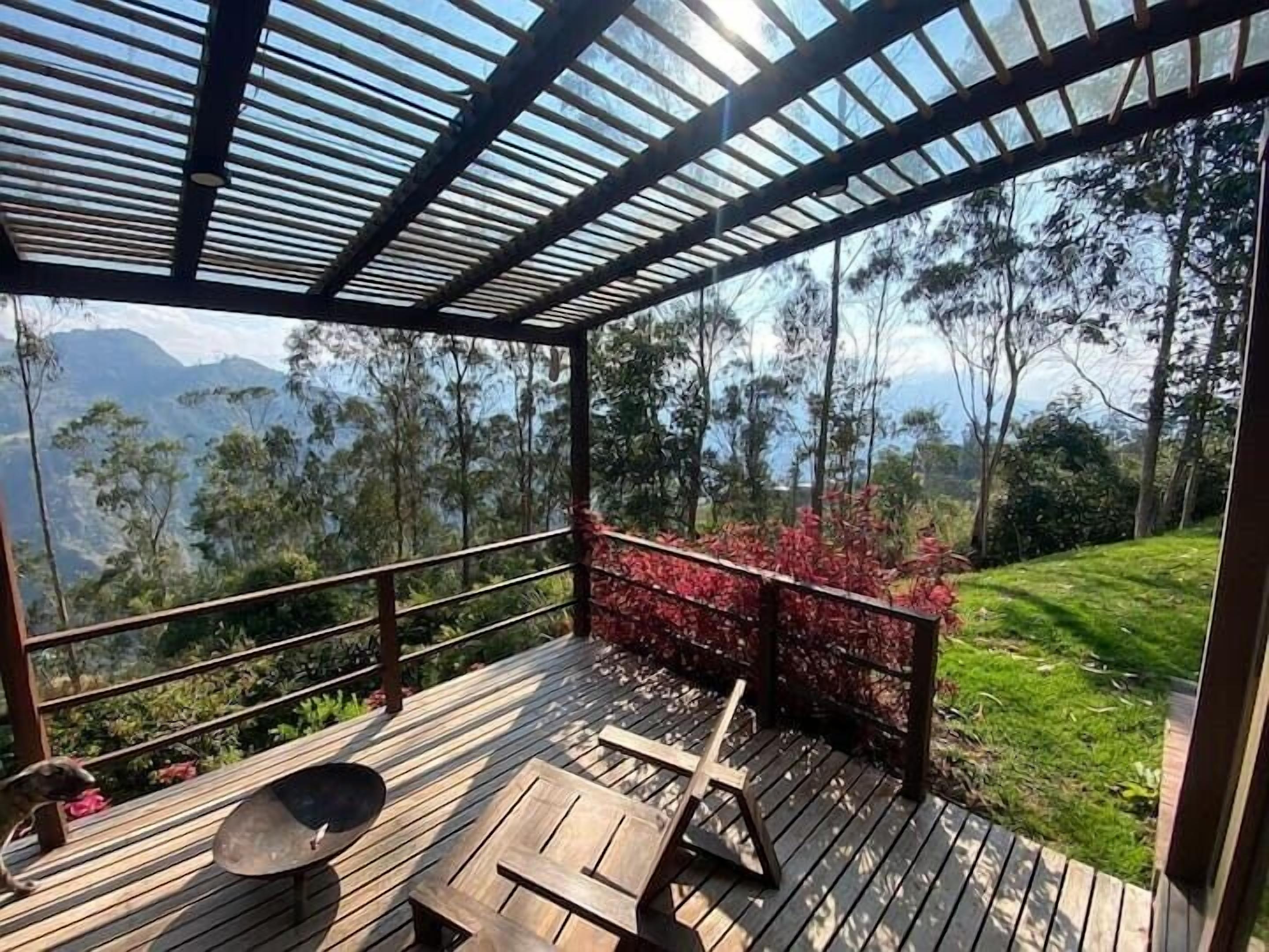 Un espace extérieur abrité doté d’une terrasse en bois, d’une rambarde en métal et offrant une vue sur un paysage montagneux.