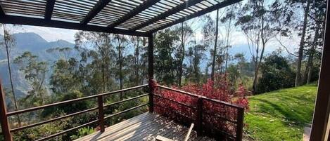 Un espace extérieur abrité doté d’une terrasse en bois, d’une rambarde en métal et offrant une vue sur un paysage montagneux.
