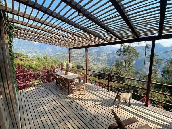 Eine Holzterrasse mit Tisch und Stühlen, mit Blick auf eine gebirgige Landschaft.
