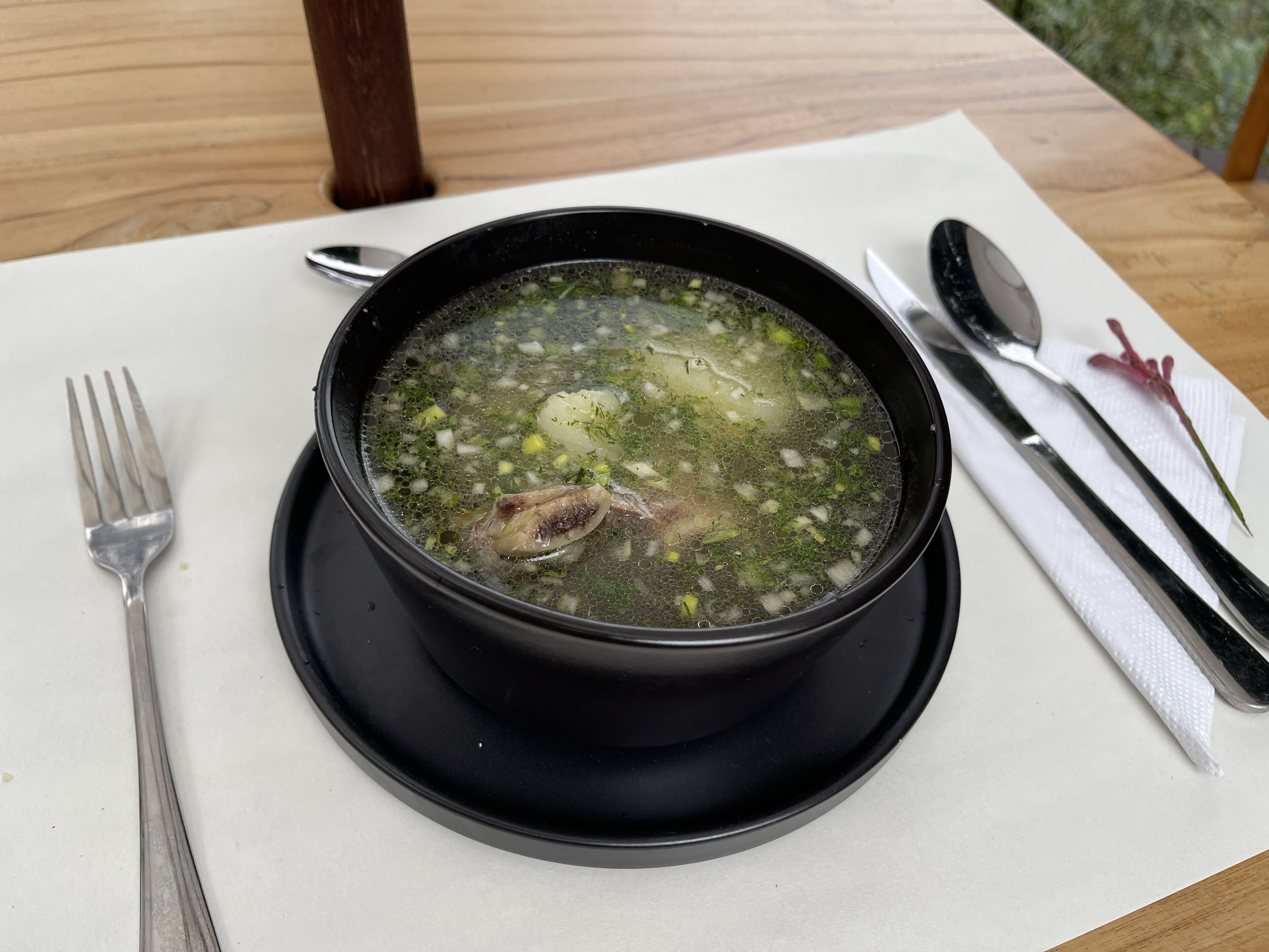 Eine Schüssel Suppe auf einem weißen Tisch, daneben ein Messer und eine Gabel auf einer Serviette.