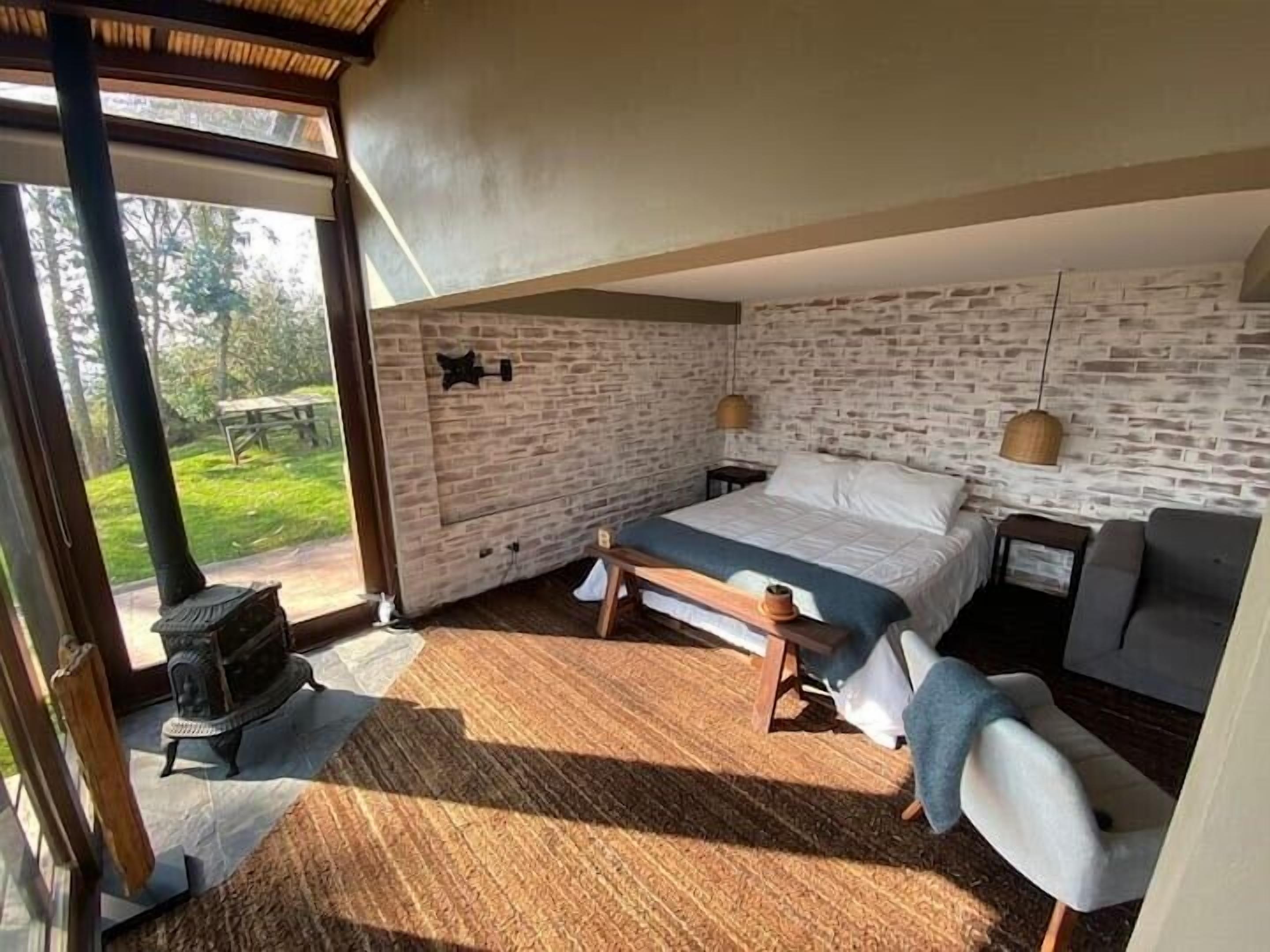 A bedroom with a stone wall, a bed, a bench, a chair, and a fireplace.