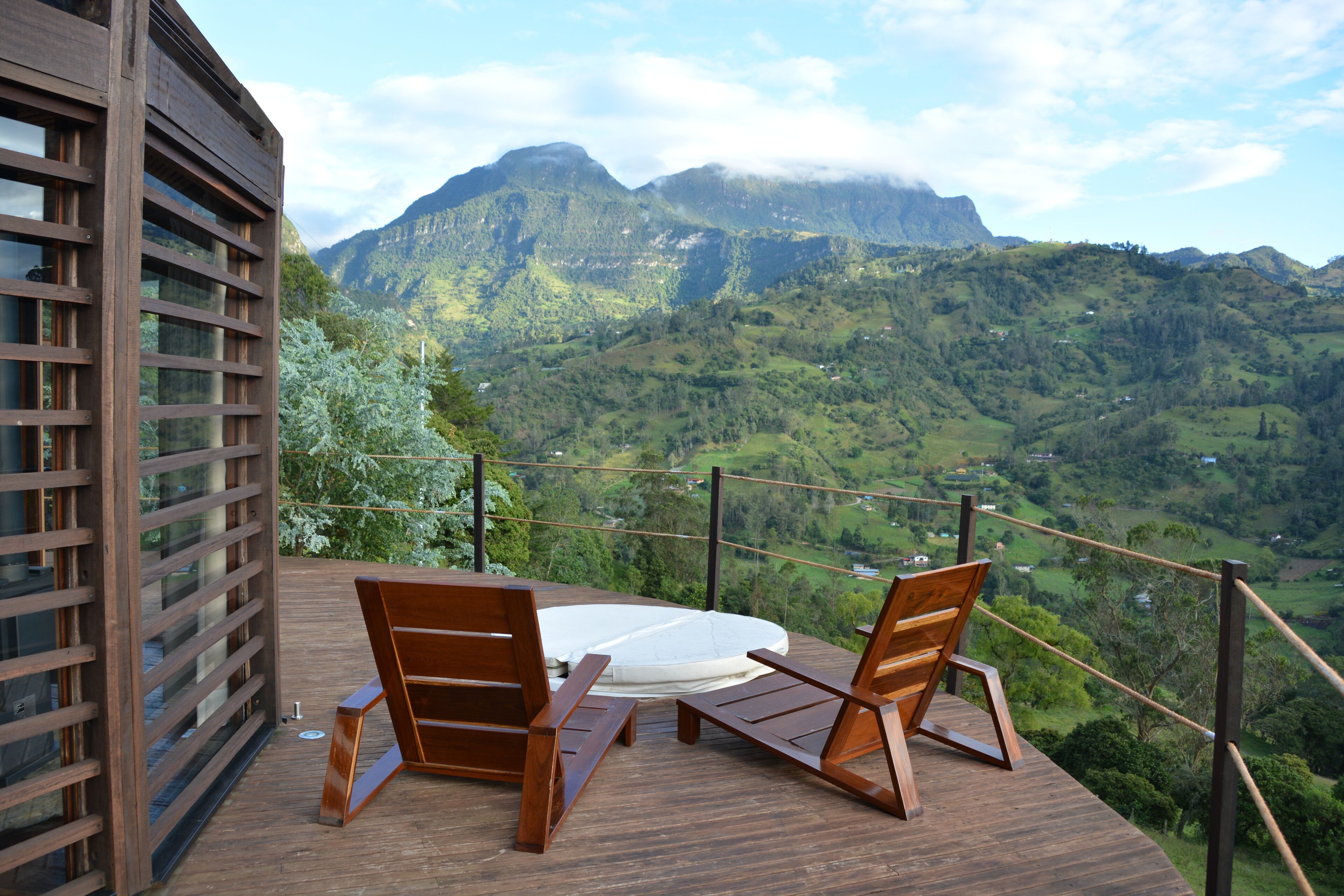 Eine Holzterrasse mit zwei Stühlen und einem runden Tisch, mit Blick auf eine gebirgige Landschaft.