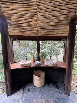 Eine Holzhütte mit einem gewobenen Dach, einer Bank mit Blumentöpfen und einem Steinfußboden.