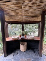 A wooden structure with a woven roof, a bench with potted plants, and a stone floor.