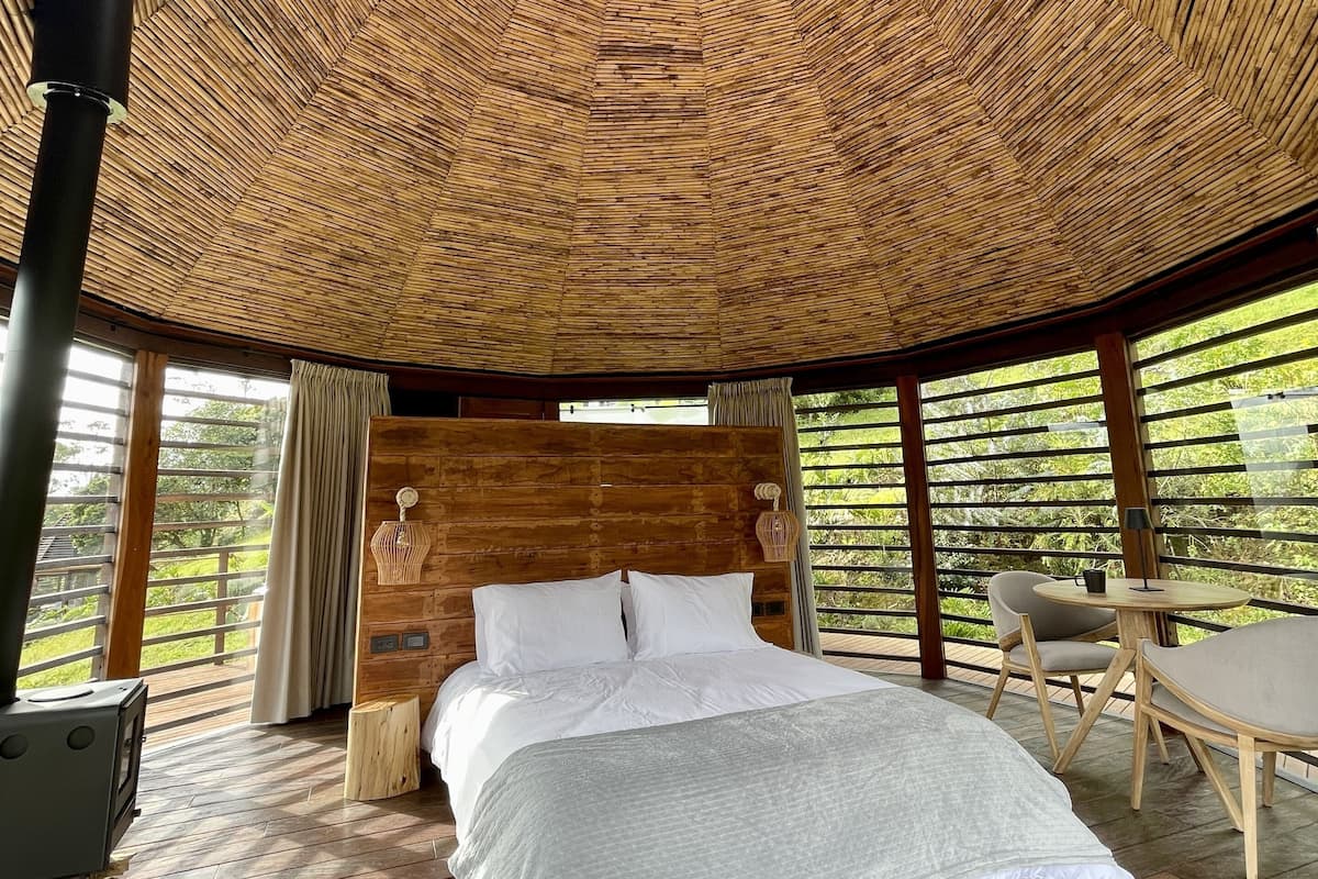 Een kamer met een groot bed, een houten hoofdbord en uitzicht op groen.