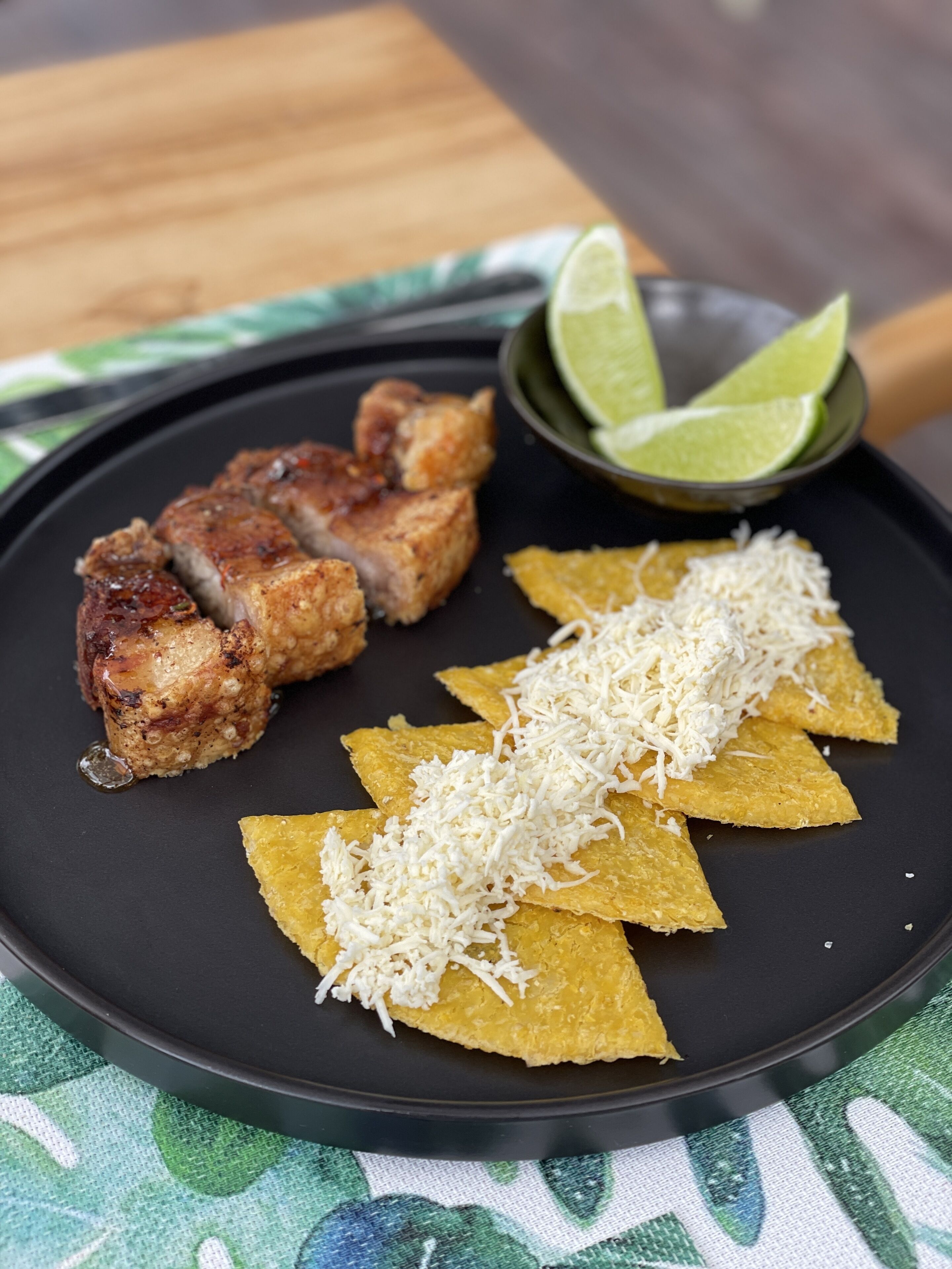 Une assiette de viande grillée, de chips de tortillas et de quartiers de citron vert.
