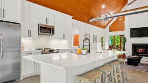 A modern kitchen with white cabinets, stainless steel appliances, and a large island with bar stools. - Luxe Pool Retreat for Couples and Small Groups (Broken Bow)