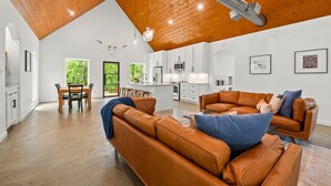 A spacious living area with a high ceiling, a dining table, and a kitchen in the background. - Luxe Pool Retreat for Couples and Small Groups (Broken Bow)