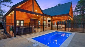 A log cabin with a swimming pool, wooden exterior, and a fenced deck area. - Luxe Pool Retreat for Couples and Small Groups (Broken Bow)
